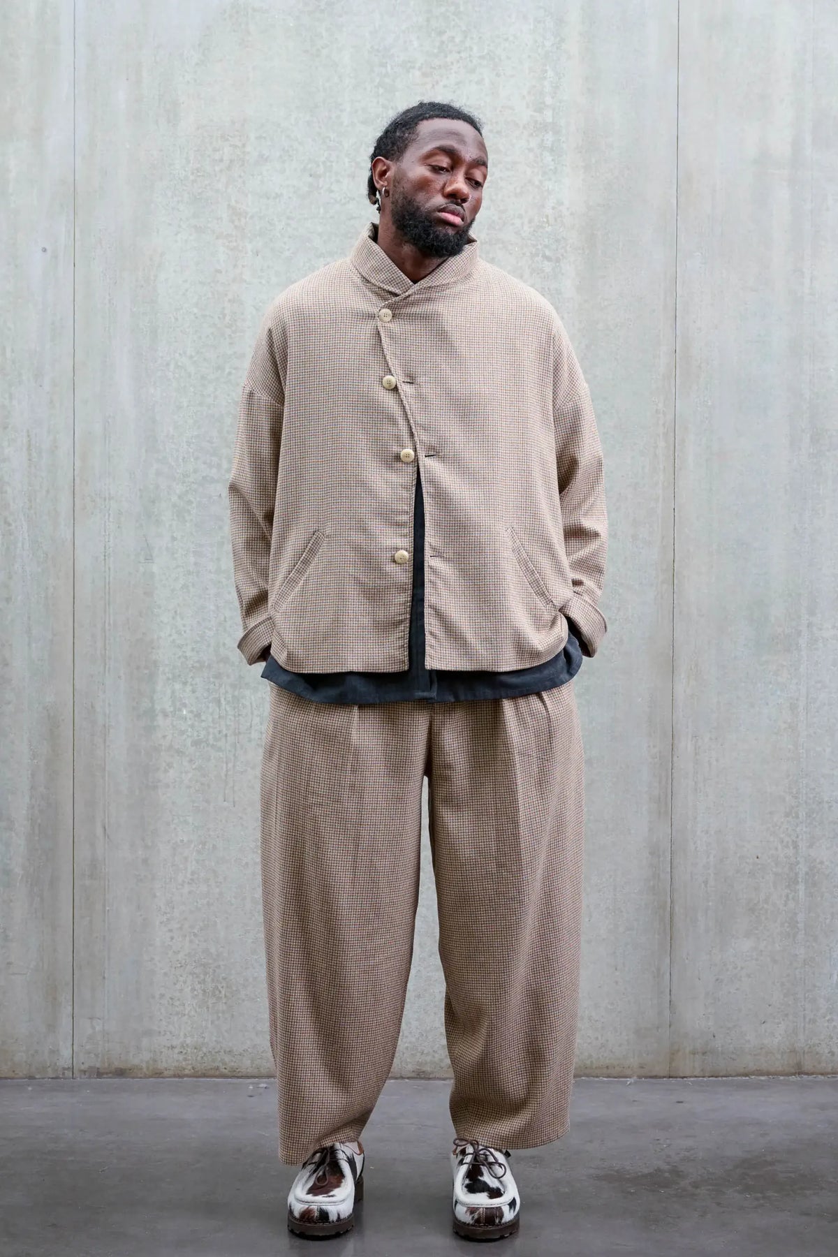 Pantalon circulaire unisexe de la marque Aïdama, coupe ballon en laine marron à motif pied de poule. Porté par un mannequin homme et vu de face.