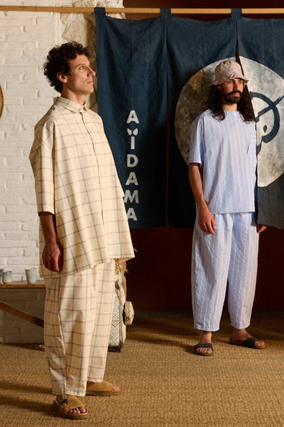 Pantalon circulaire de la marque Aïdama, coupe ballon en coton crème à carreaux. Porté par un mannequin homme et vu de profil.