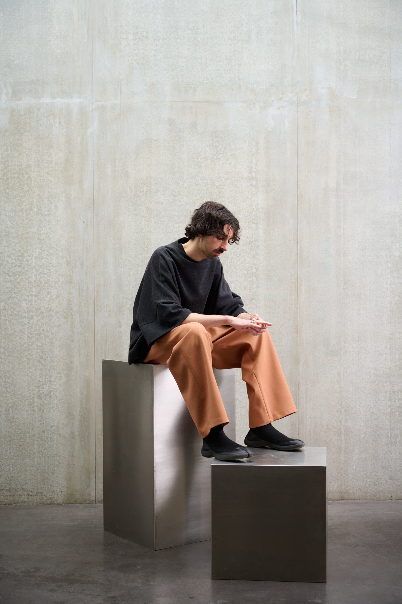 Pantalon droit de la marque Aïdama coupe oversize en laine et coton orange. Porté par un mannequin homme, vu de profil assis.