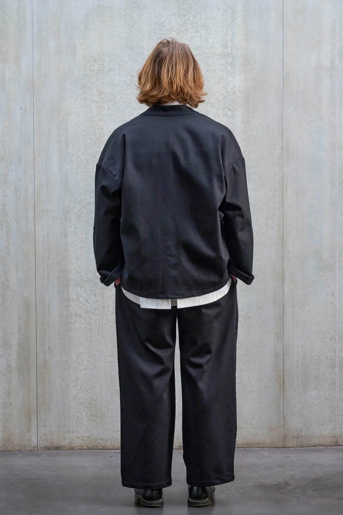 Pantalon droit unisexe de la marque Aïdama, coupe oversize en sergé de coton noir. Porté par un mannequin homme et vu de dos.