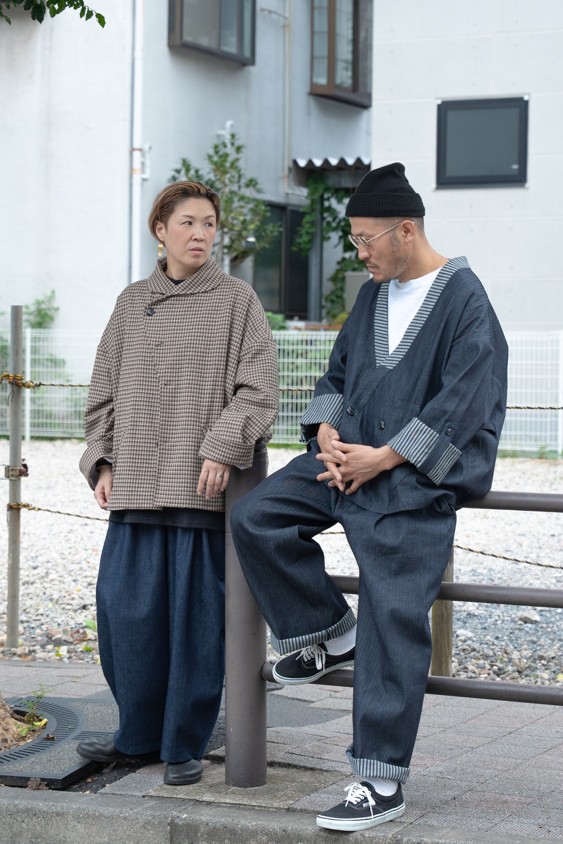 Pantalon droit Aïdama, coupe oversize en denim japonais rayé. Porté par un mannequin homme assis sur une barrière dans une rue japonaise et vu de face.
