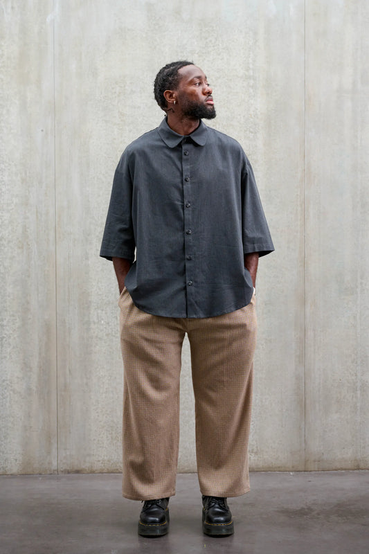 Pantalon droit de la marque Aïdama, coupe ample en laine marron à motif pied de poule. Porté par un mannequin homme et vu de face.
