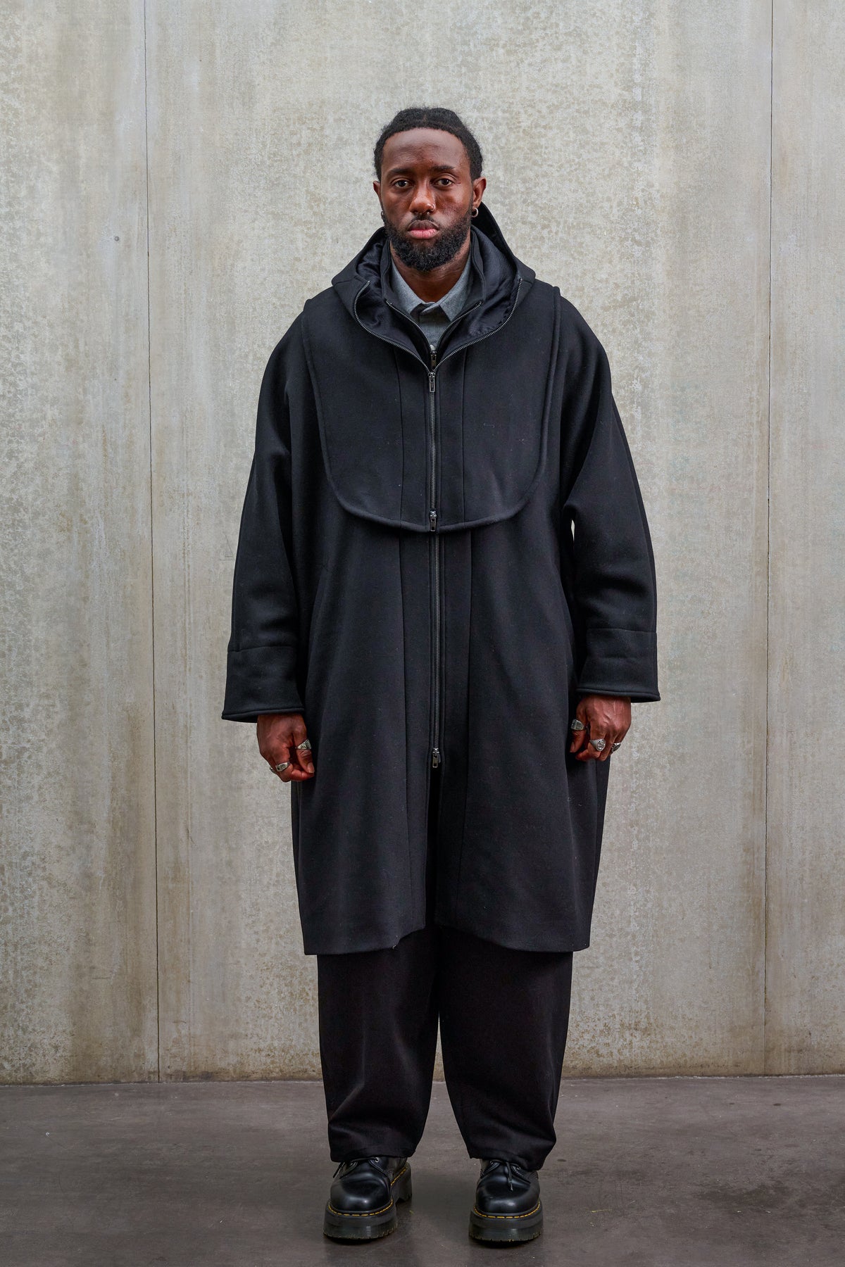 Plastron à capuche de la marque Aïdama, modèle Do en drap de laine noir double face. Porté fermé par un mannequin homme et vu de face.