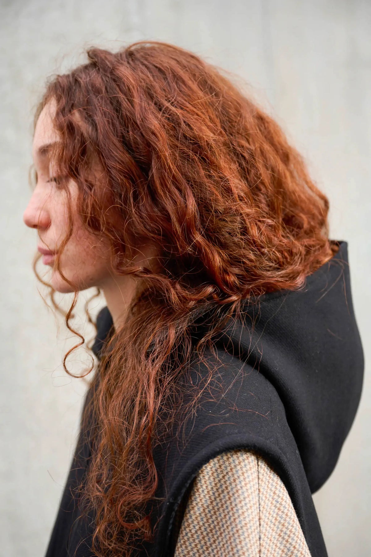Plastron à capuche de la marque Aïdama, modèle Do en sergé de laine noir. Porté fermé par une mannequin femme et vu de profil.