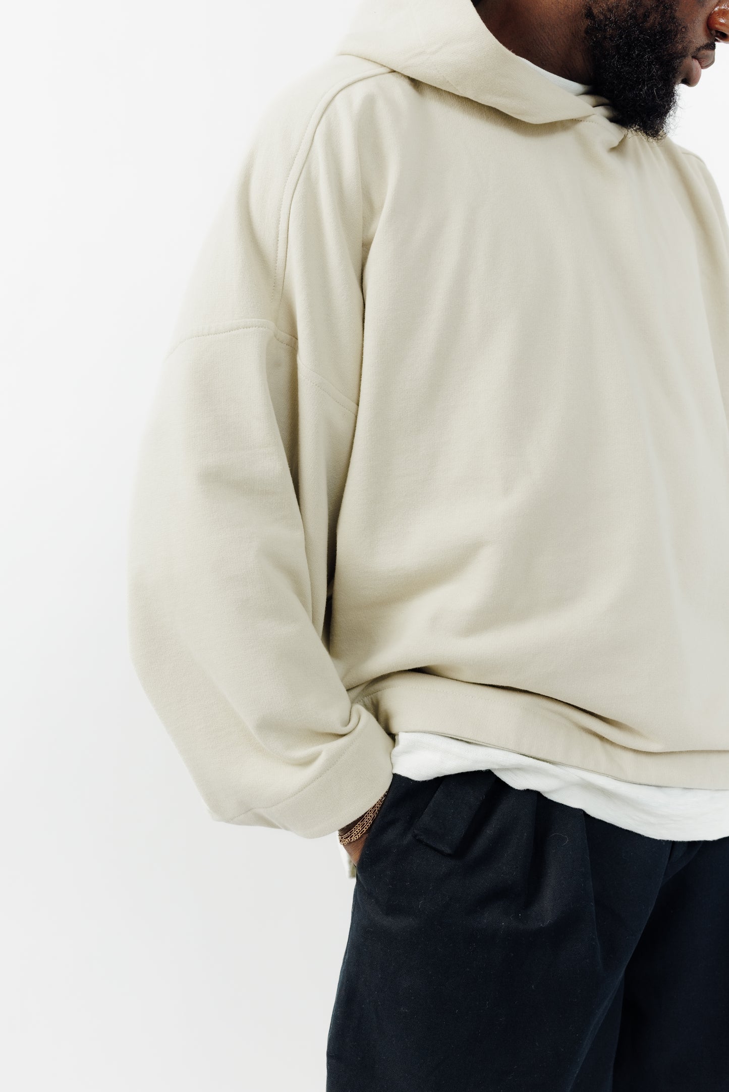 Sweat à capuche oversize Mino de la marque Aïdama en molleton de coton beige. Porté par un mannequin homme et vu zoomé sur la manche. 