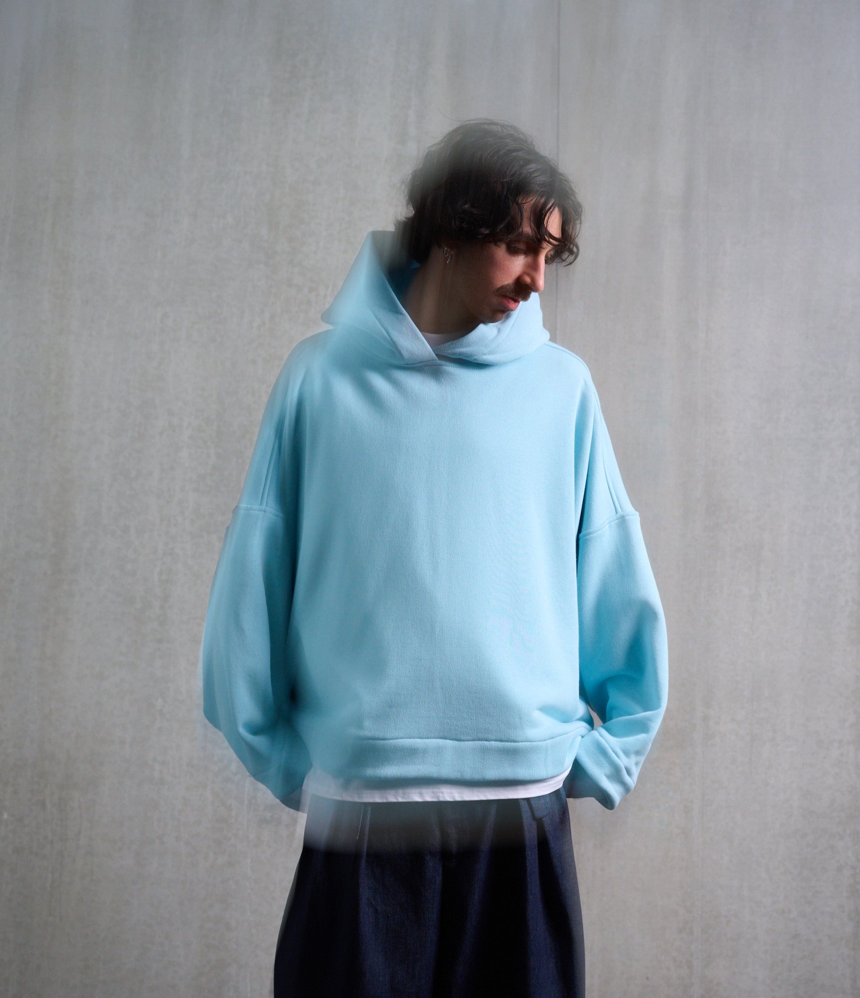 Sweat à capuche oversize en molleton de coton bleu pâle Mino de la marque Aïdama. Porté capuché par un mannequin homme et vu de face.