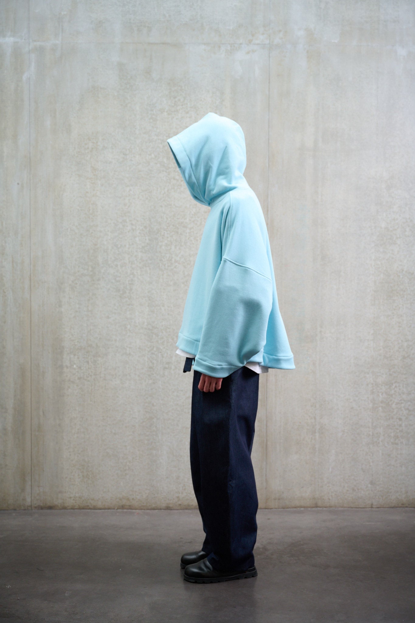 Sweat à capuche oversize en molleton de coton bleu pâle Mino de la marque Aïdama. Porté capuché par un mannequin homme et vu de profil.