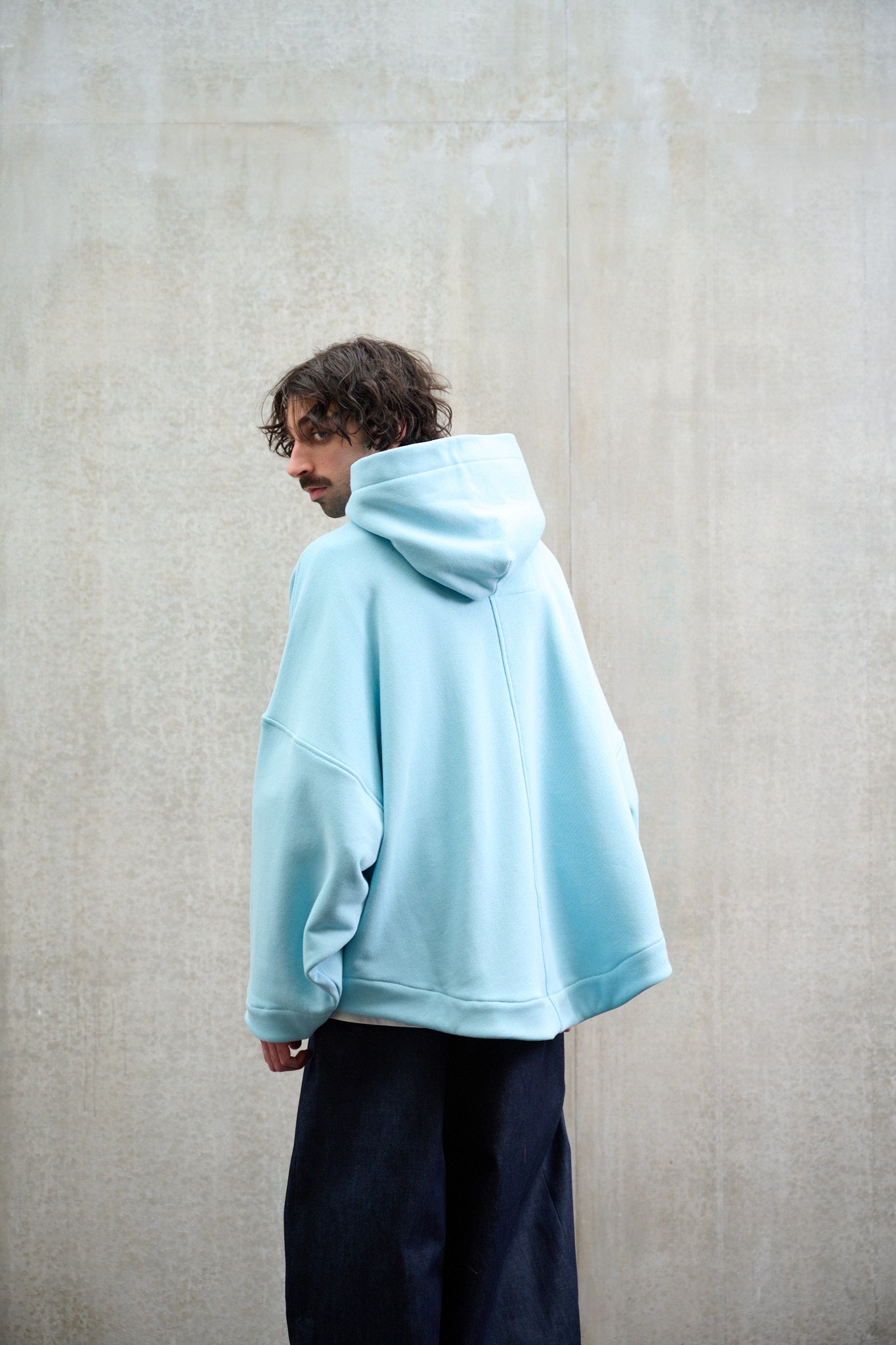 Sweat à capuche oversize en molleton de coton bleu pâle Mino de la marque Aïdama. Porté par un mannequin homme et vu de dos.
