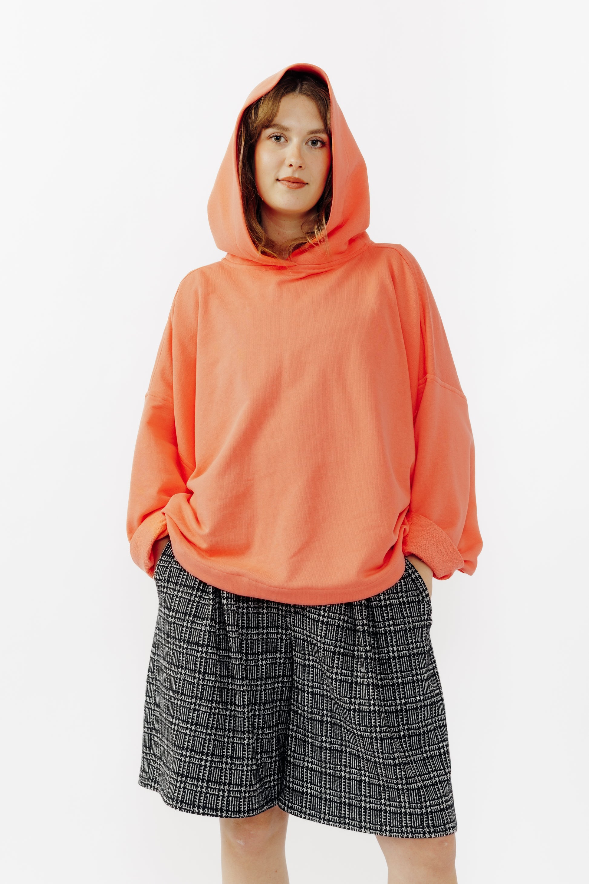 Sweat à capuche oversize Mino de la marque Aïdama en molleton de coton corail. Porté capuche relevéepar une mannequin femme et vu de face. 