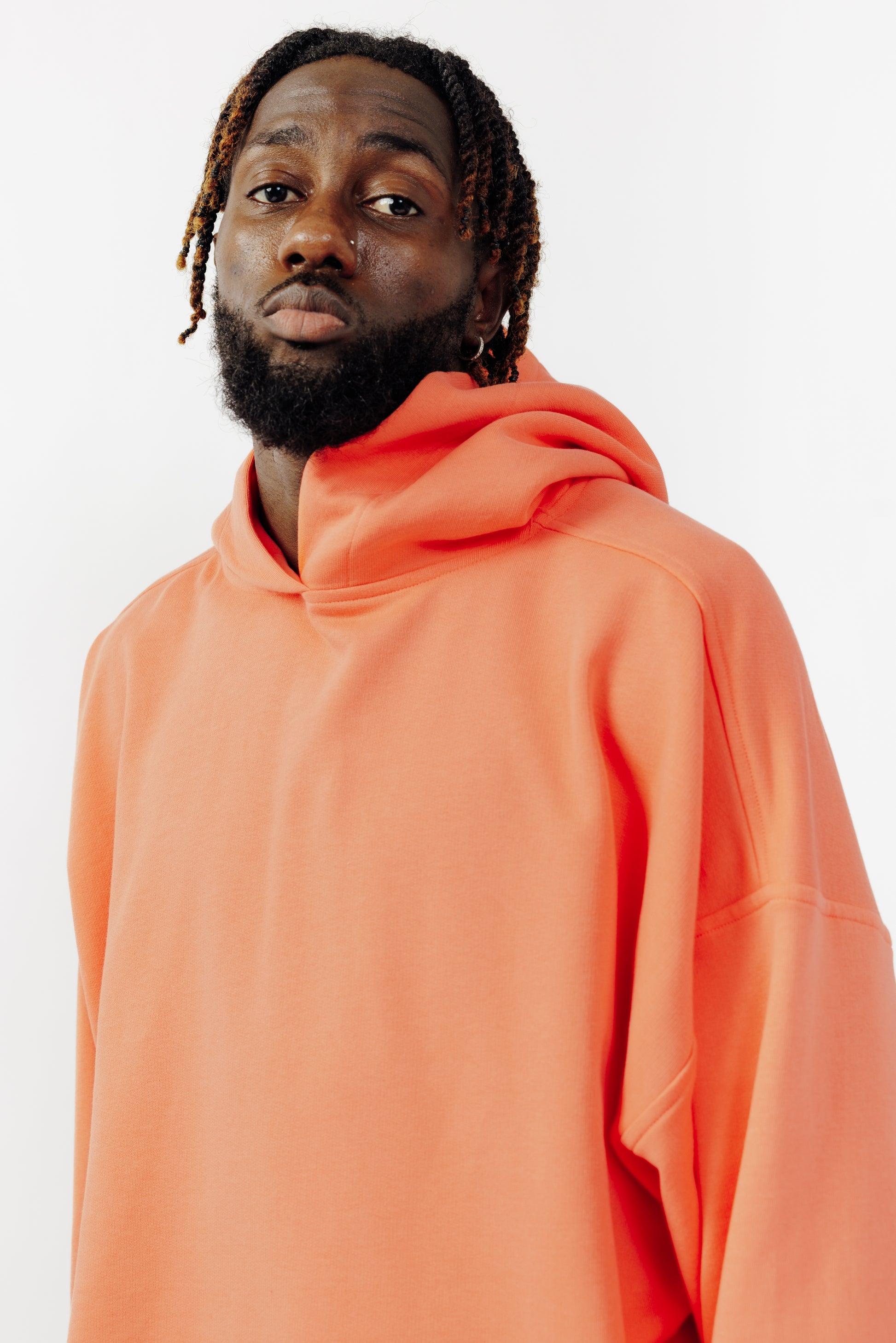 Sweat à capuche oversize Mino de la marque Aïdama en molleton de coton corail. Porté par un mannequin homme et vu de face zoomé sur le buste.