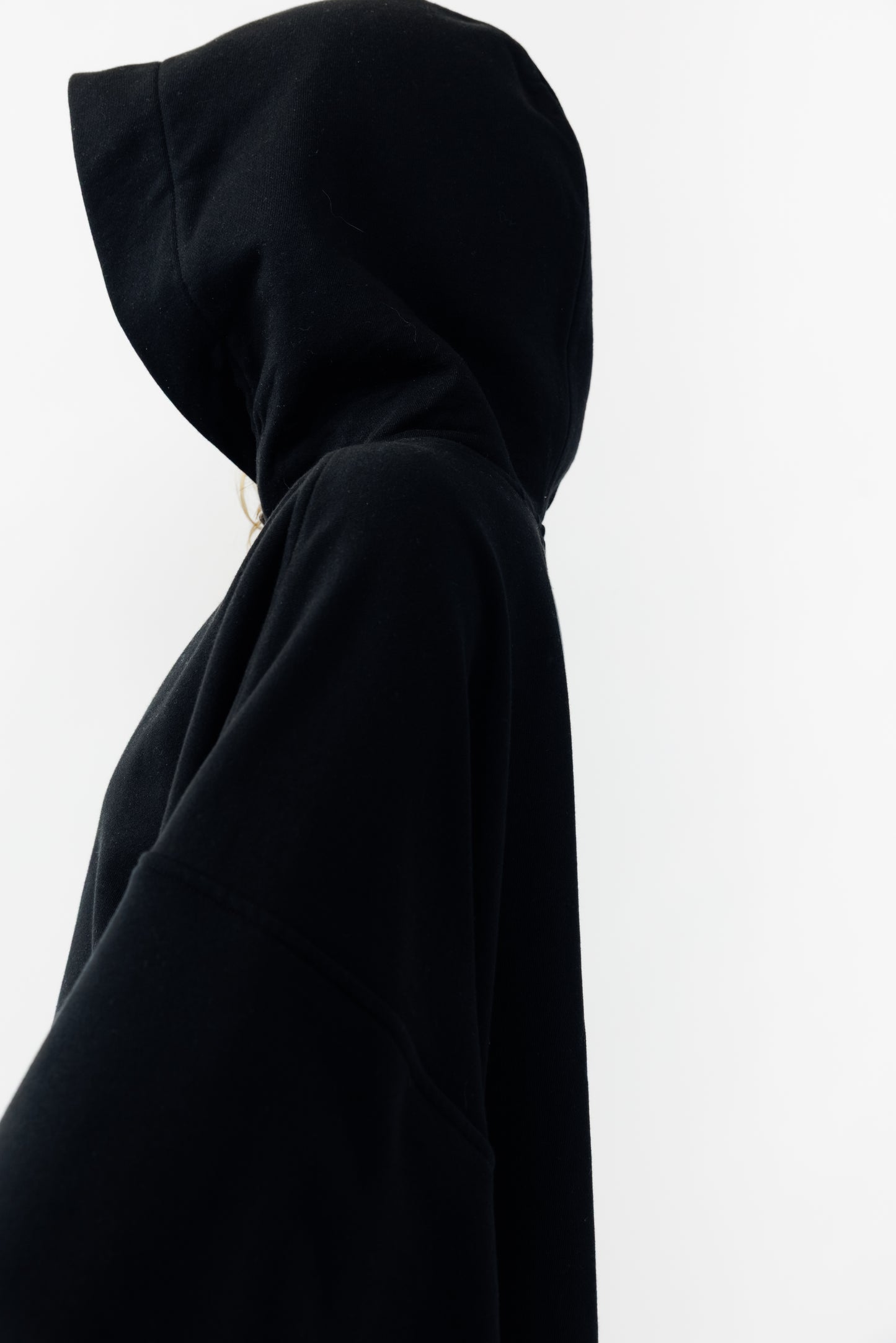 Sweat à capuche oversize Mino de la marque Aïdama en molleton de coton noir. Porté encapuchonné par une mannequin femme et vu de profil. 