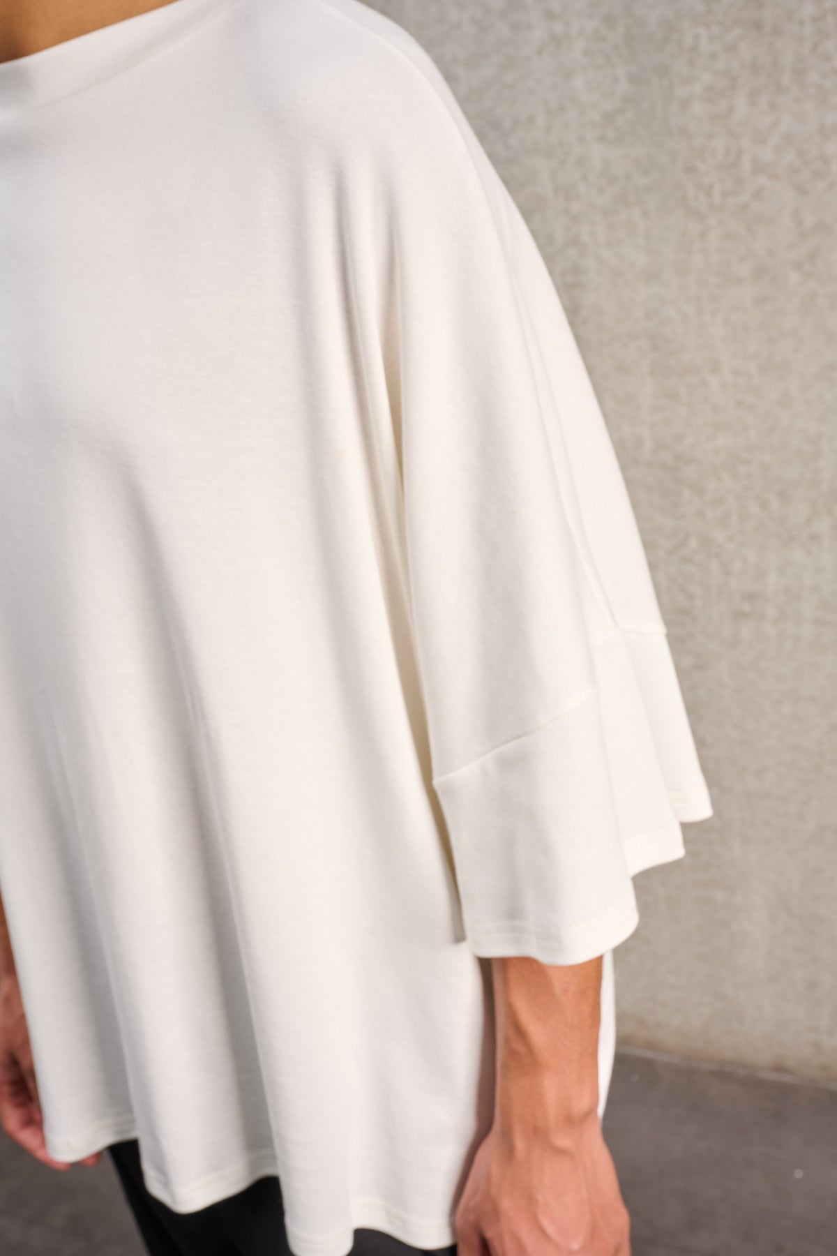T-shirt oversize à col bateau de la marque Aïdama, modèle Haku en jersey de coton blanc certifié GOTS. Porté par un mannequin homme et vu zoomé sur la manche.