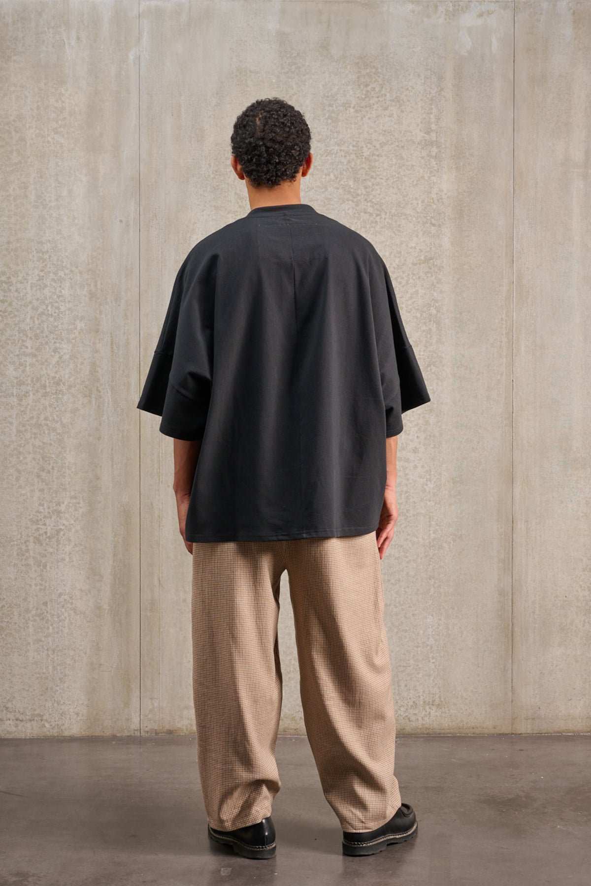T-shirt oversize à col bateau de la marque Aïdama, modèle Haku en jersey de coton noir épais. Porté par un mannequin homme et vu de dos.
