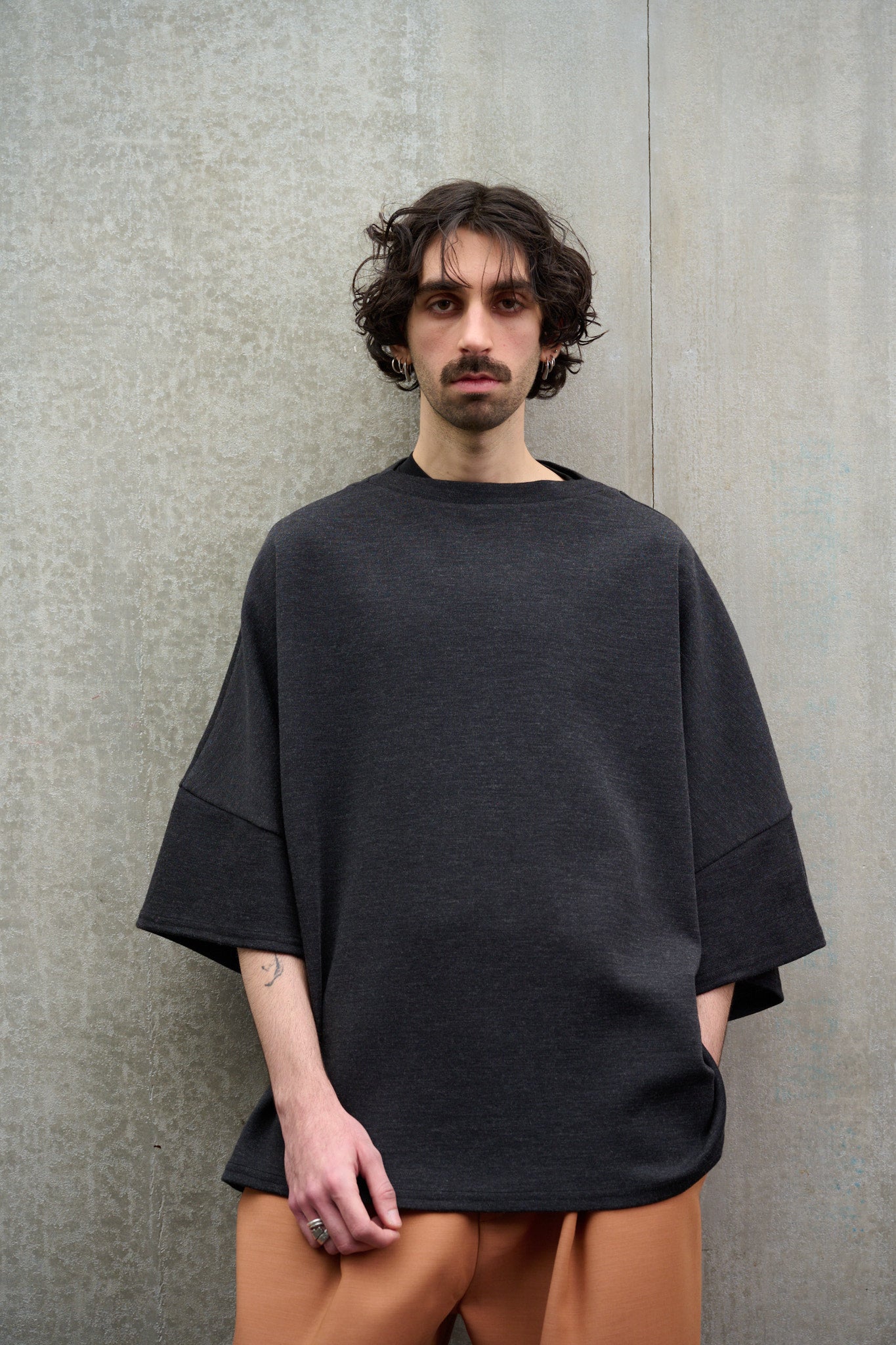 T-shirt oversize à col bateau Haku en laine gris quartz chiné de la marque Aïdama. Porté par un mannequin homme et vu de face avec une main dans la poche.