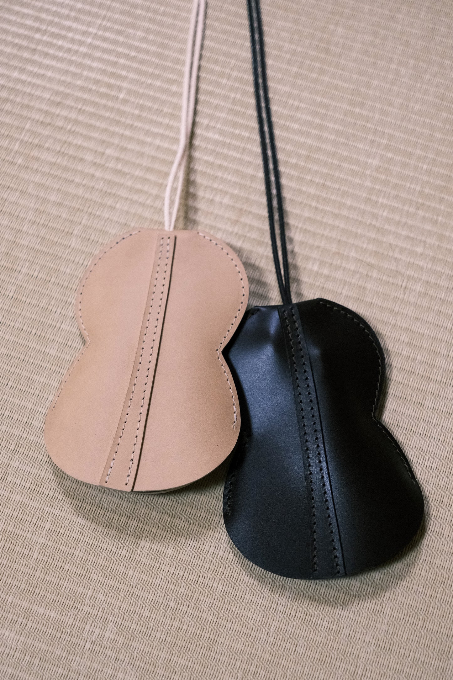 Tours de cou portes-cartes & portes-clés Hyotan de la marque Aïdama en cuir de vachette beige et acajou, posés sur un tatami et zoomés.