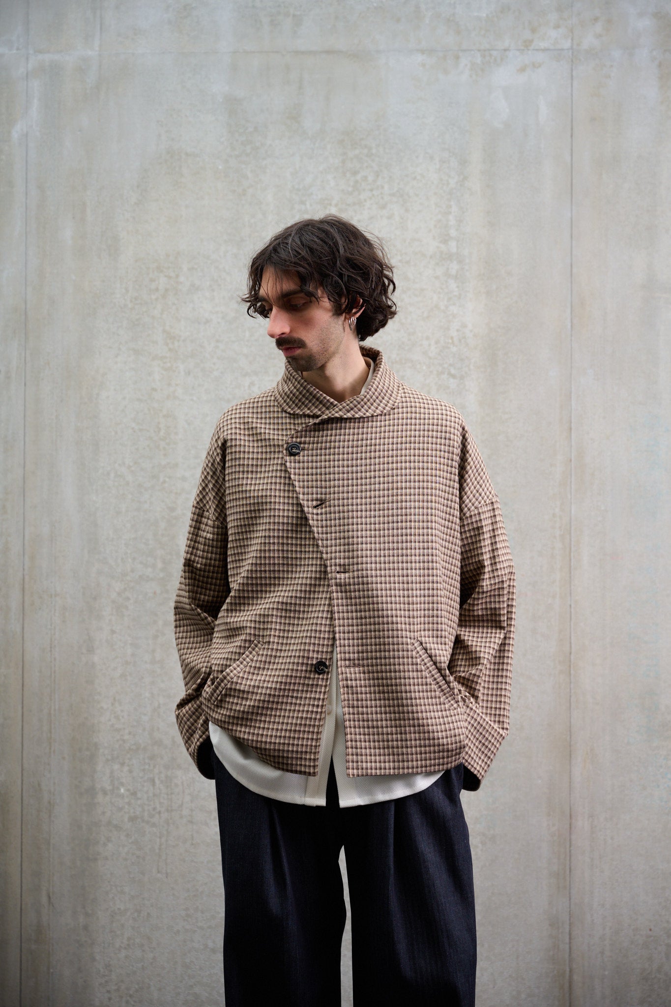 Veste oversize à col arrondi de la marque Aïdama, modèle Gunbai en laine marron à motif Vichy. Portée fermée par un mannequin homme et vue de face avec les mains dans les poches.