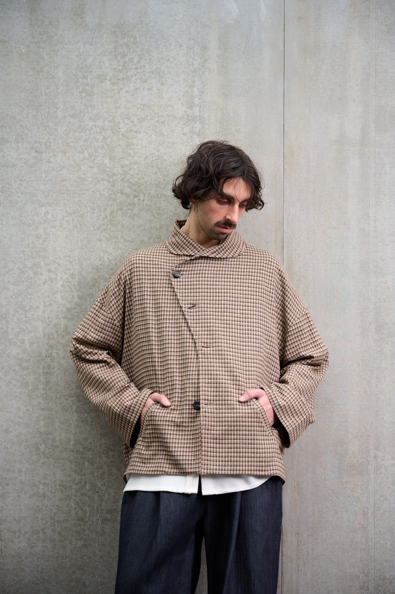 Veste oversize à col arrondi de la marque Aïdama, modèle Gunbai en laine marron à motif Vichy. Portée fermée par un mannequin homme et vue de face les mains dans les poches.