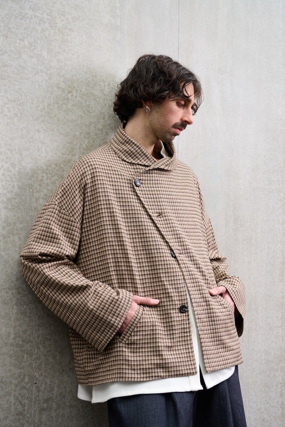 Veste oversize à col arrondi de la marque Aïdama, modèle Gunbai en laine marron à motif Vichy. Portée fermée par un mannequin homme et vue de profil.
