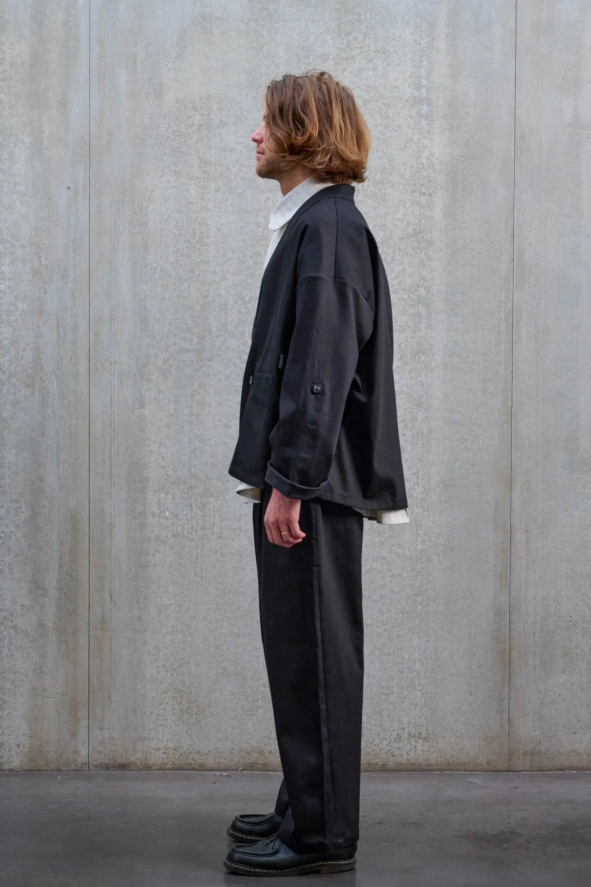 Veste oversize à col kimono de la marque Aïdama, modèle Samue en sergé de coton noir. Portée fermée par un mannequin homme et vue de profil.