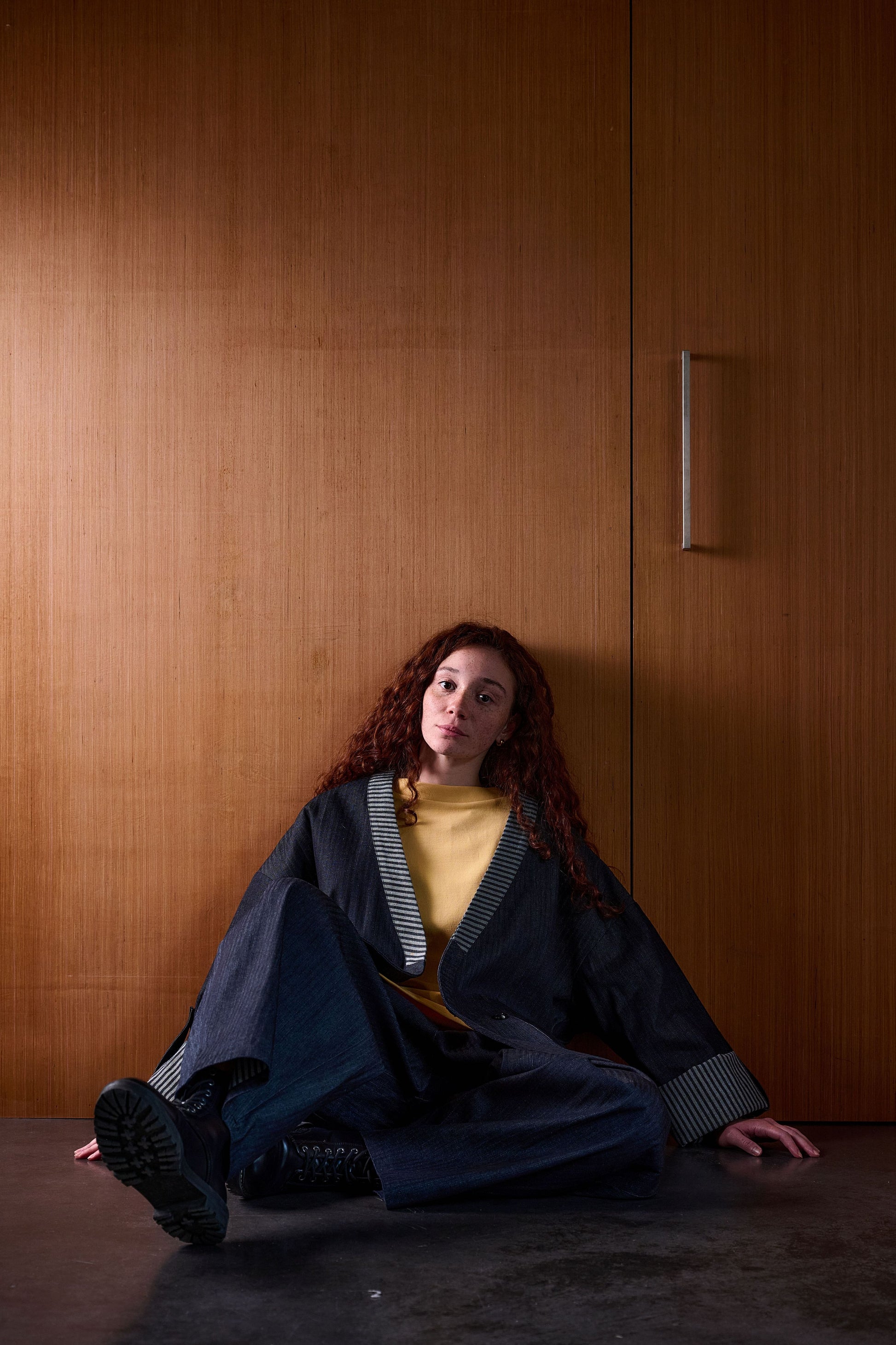 Veste croisée à col kimono Aïdama modèle samue en denim japonais brut. Portée ouverte par une mannequin femme assise et adossée à une porte.
