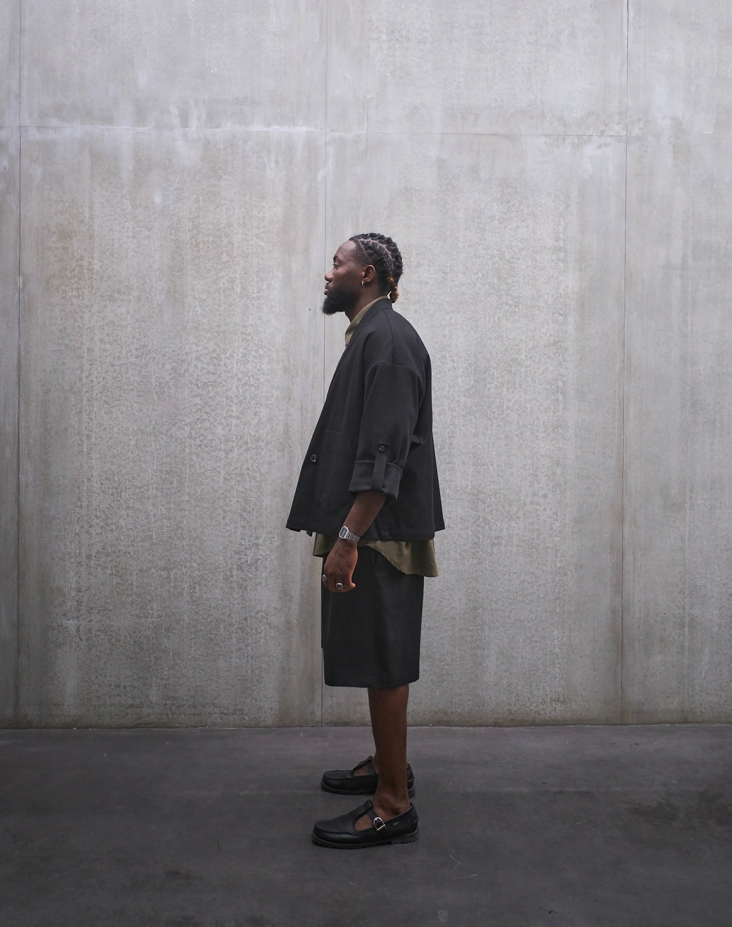 Veste croisée à col kimono Aïdama, modèle samue en coton noir à motif Prince de Galles ton sur ton. Portée ouverte par un mannequin homme et vue de profil.